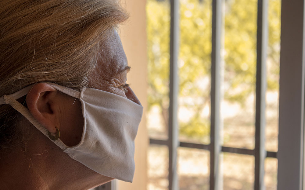 Una mujer mayor con mascarilla mira a través de una ventana.