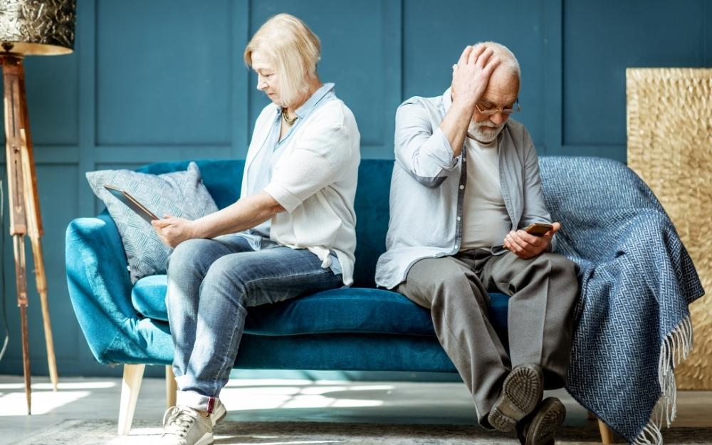 Dos personas mayores en un sofá consultan una tablet y un teléfono móvil
