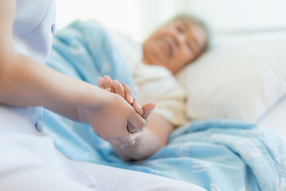 una persona mayor estirada en una cama de hospital dando la mano a otra persona