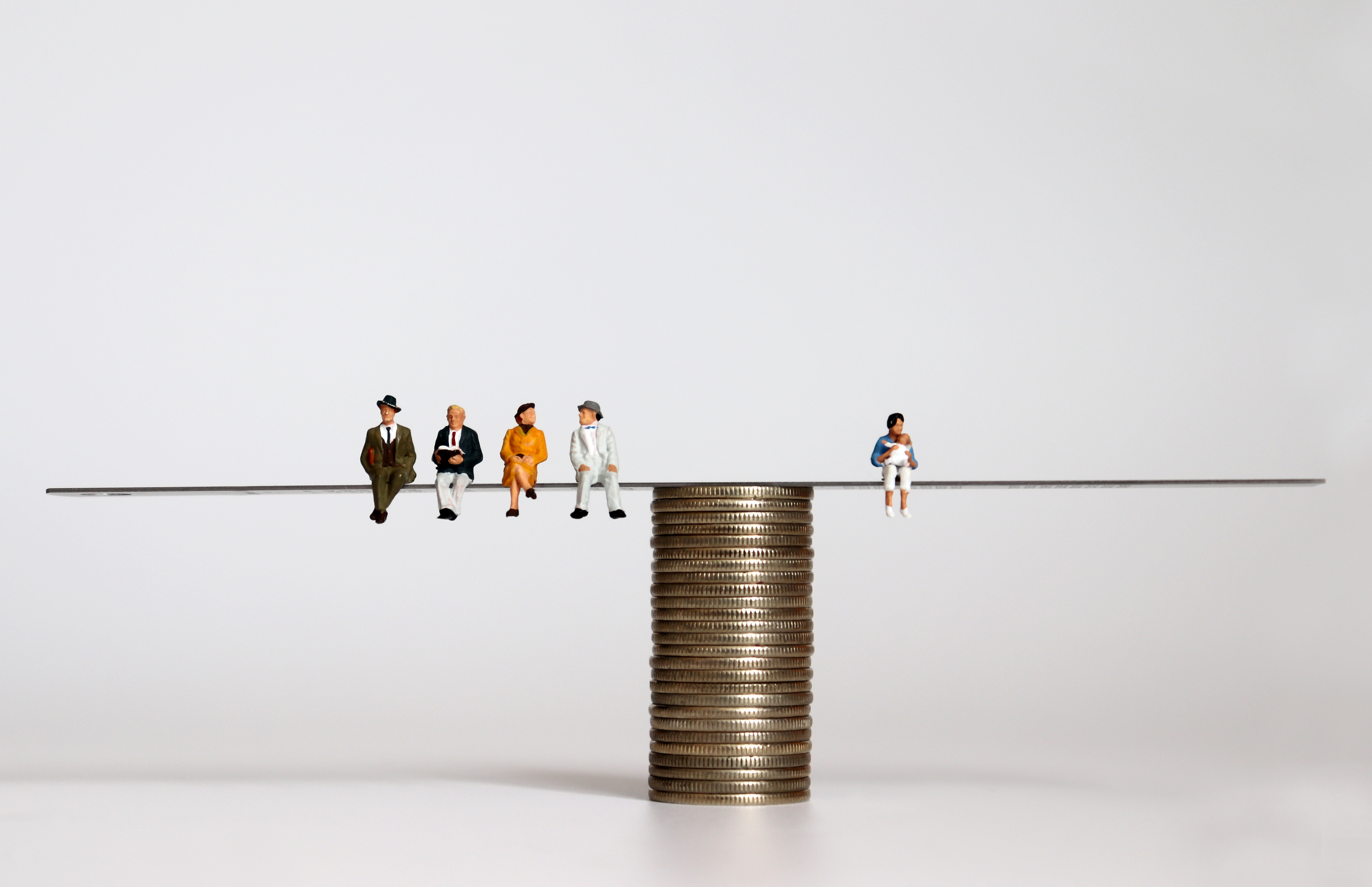 Balanza sobre monedas con una persona a la derecha que representa la población activa y al izquierda personas mayores jubiladas