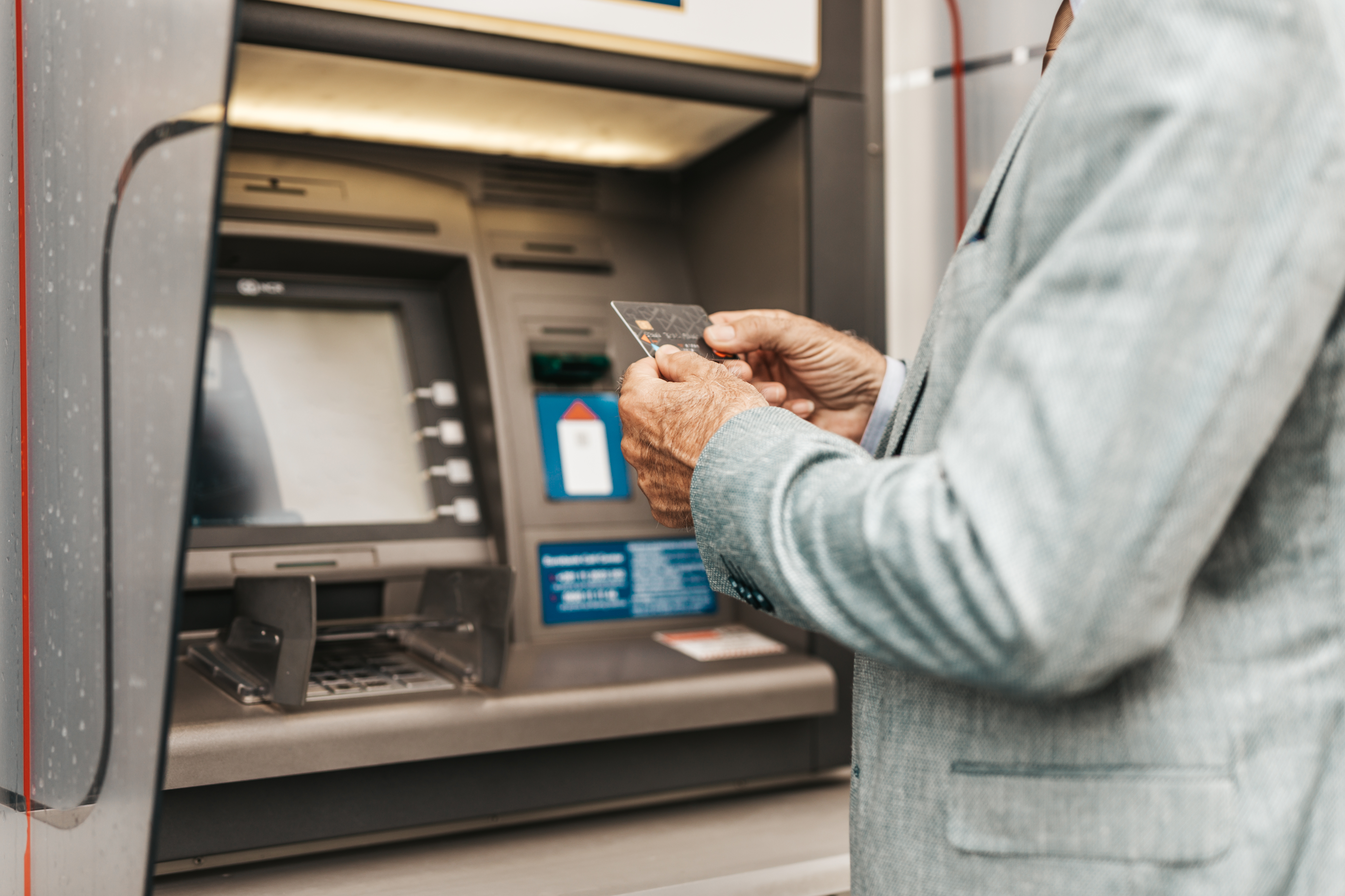 Manos de una persona mayor sujetando una tarjeta de crédito, delante de un cajero automático