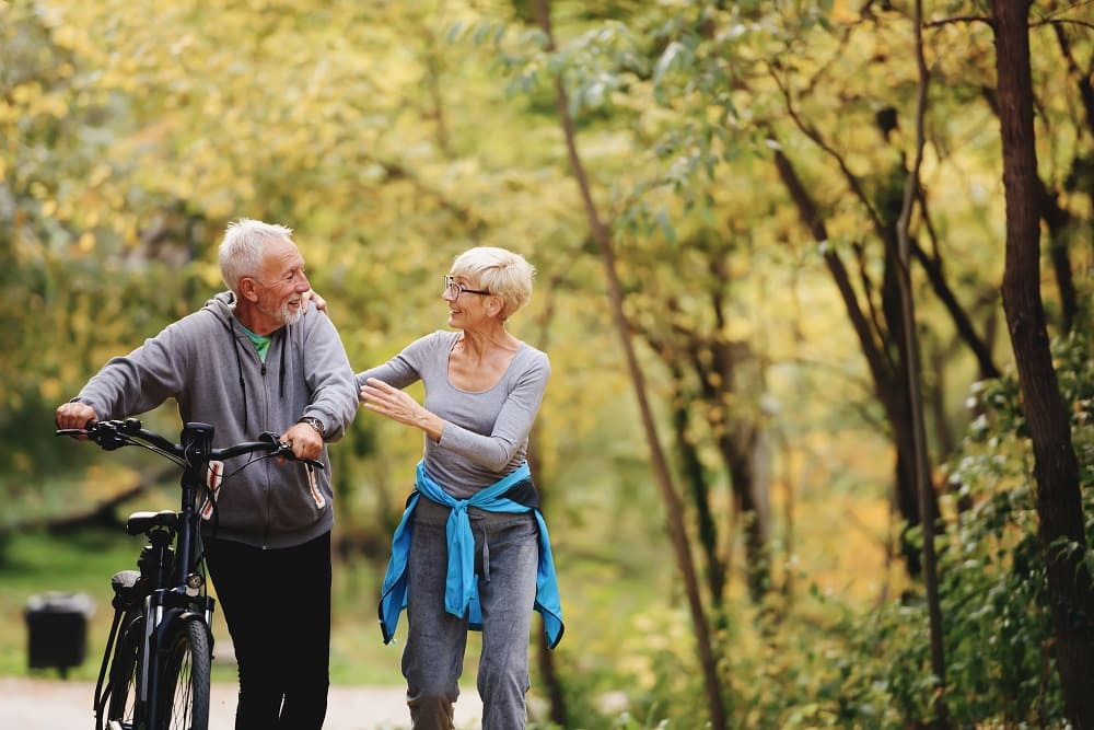 un hombre y una mujer paseando por el bosque con una bicicleta