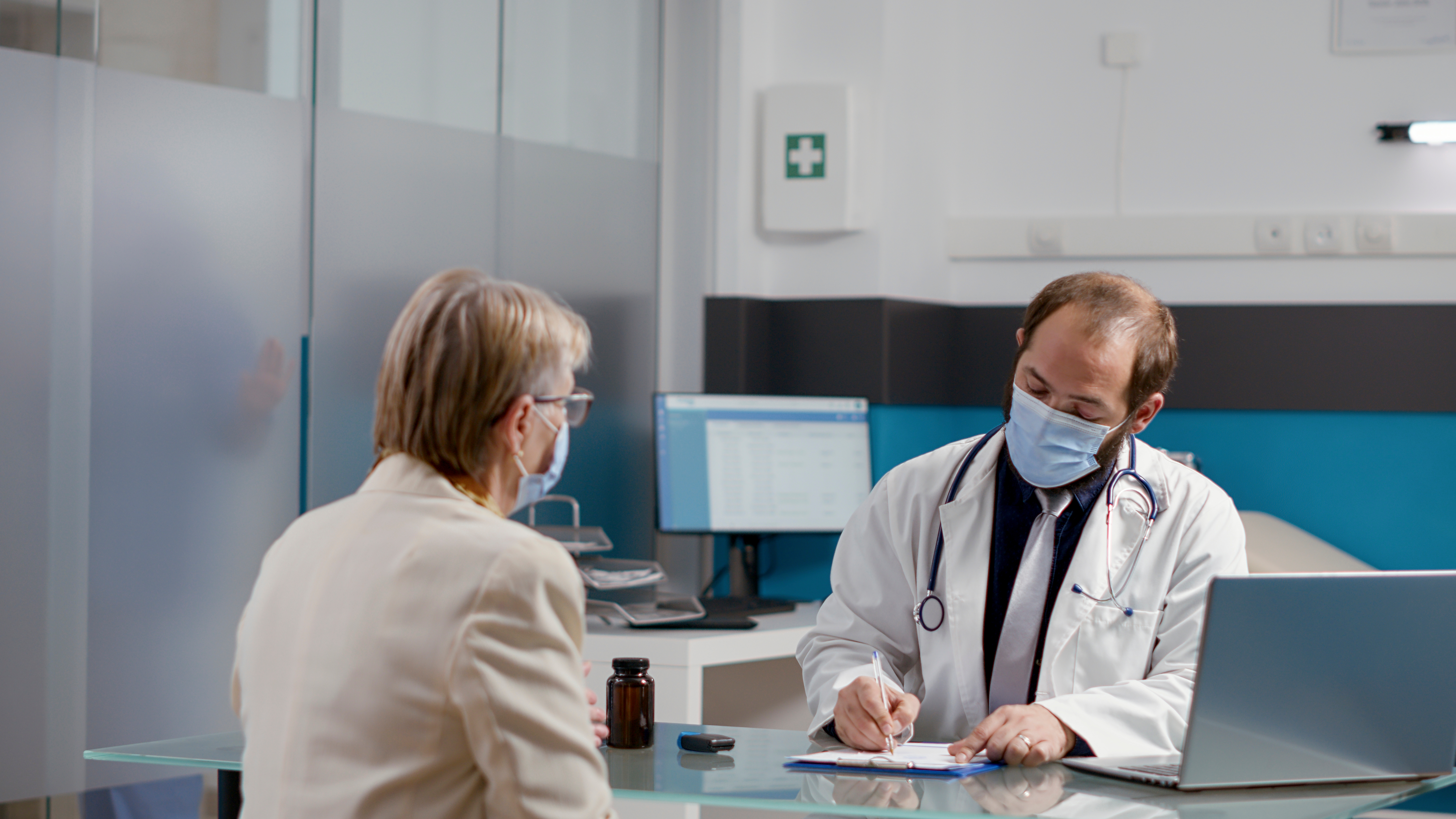 Imagen donde aparece un médico y un paciente en una consulta médica. El médico está escribiendo en un papel y la paciente observando lo que escribe. 