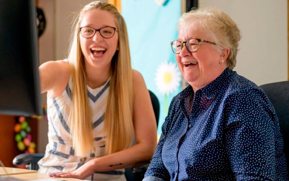 Una Mujer mayor y una mujer joven sonríen frente a la pantalla de un ordenador