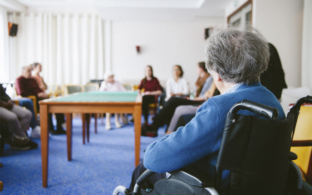 Solicita la aprobación de una declaración institucional que apoye la creación de una Convención de Naciones Unidas sobre los Derechos de las Personas Mayores. Varias personas mayores reunidas en una sala