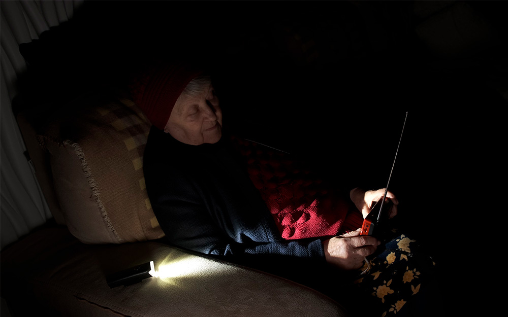 Una mujer sentada sostiene en sus manos un transistor de radio mientras se ilumina con una lintarna 