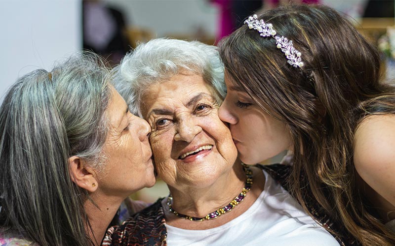 Día Internacional de la Mujer Dos mujeres besan en las mejillas a una mujer mayor.