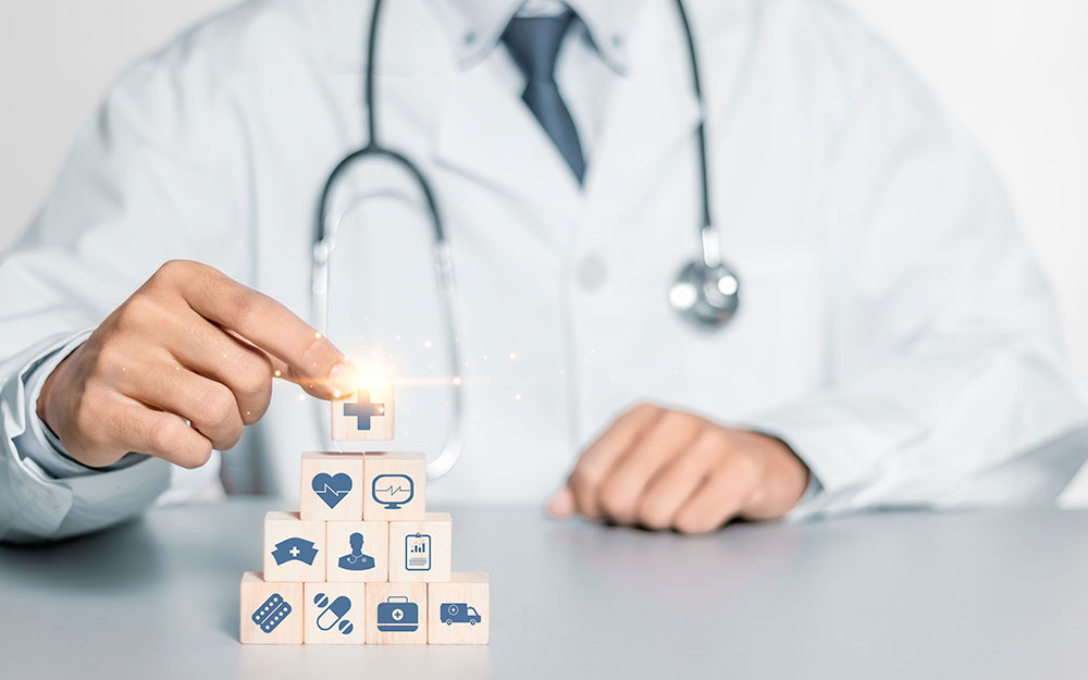 Una persona con bata de médico monta una pirámide de bloques de madera con iconos relacionados con la salud