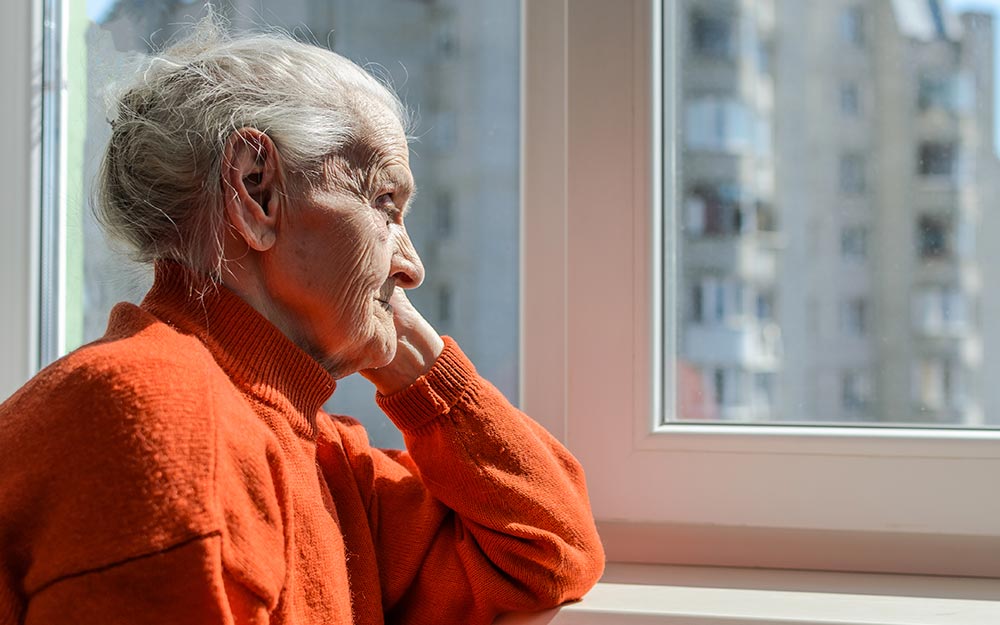 Insta a emprender políticas públicas cuyo objetivo sea el bienestar de las personas, los hogares y las familias Una mujer mayor mira a través de una ventana.