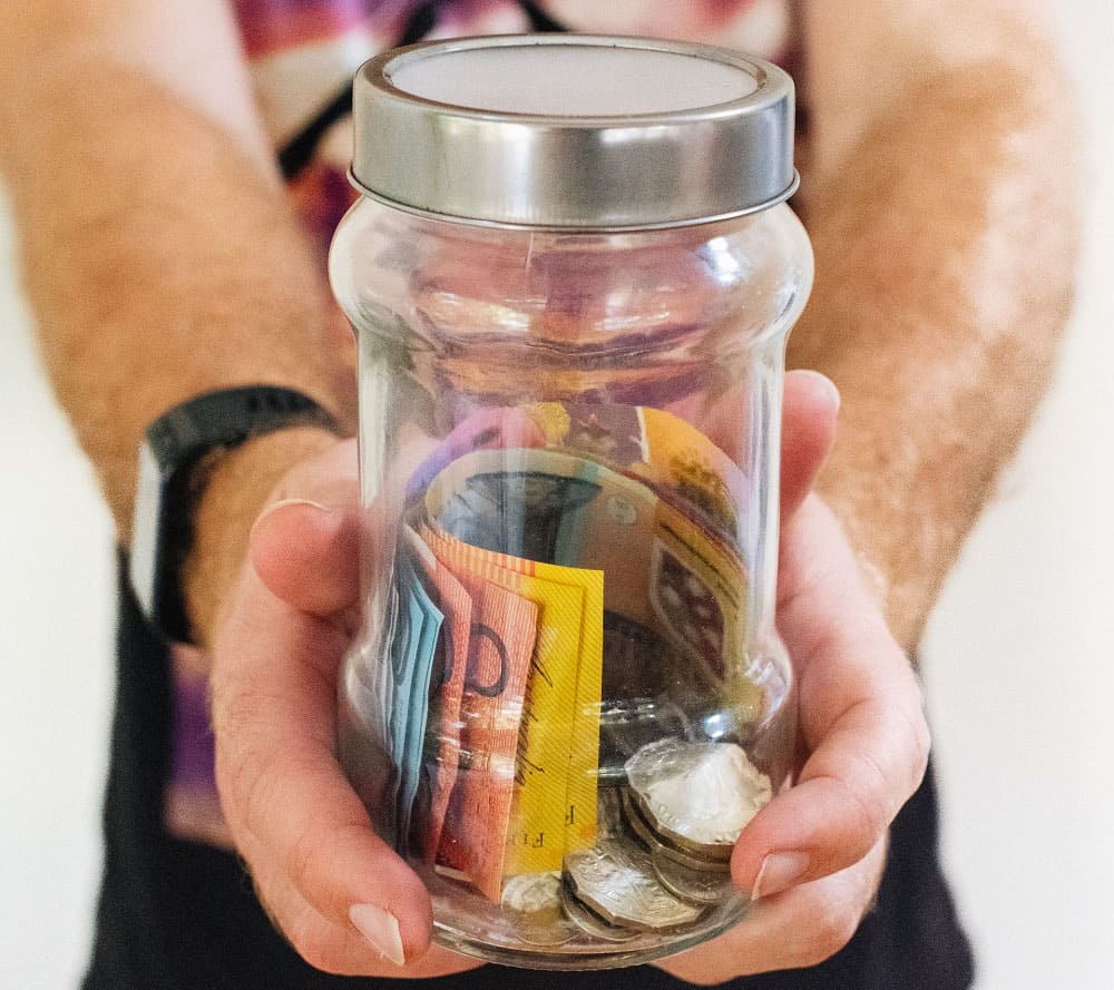 Unas manos sujetando un bote de cristal con dinero en el interior