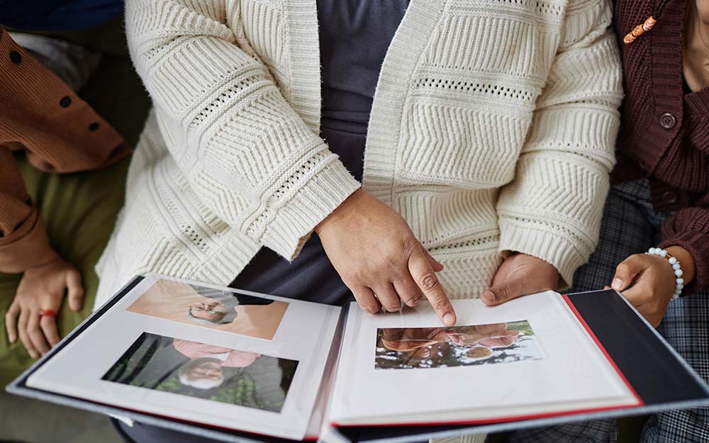 Una persona mayor enseña un álbum de fotos a otras dos personas