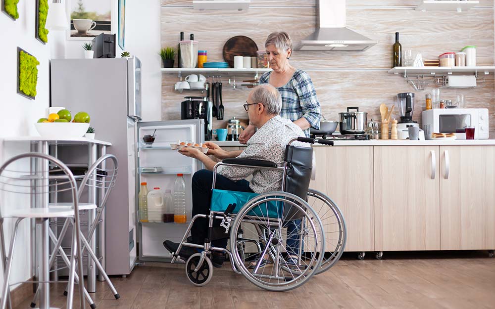 3 de diciembre: Día Internacional y Europeo de las Personas con Discapacidad Una persona en silla de ruedas saca alimentos de una nevera acompañado por una mujer.