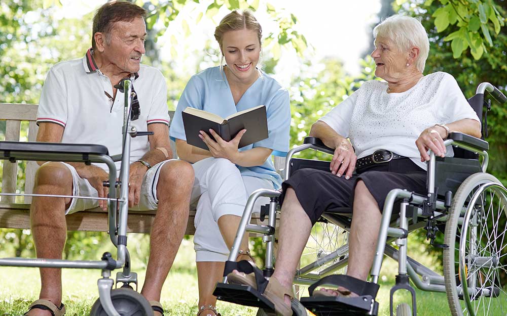 Una cuidadora lee un libro a dos personas mayores.