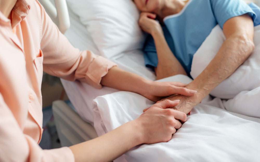 La PMP considera prioritarias las garantías de accesibilidad, proximidad y apertura de los servicios de atención primaria de salud. Una persona sujeta la mano de una persona mayor que aparecen tumbada en la cama de un hospital
