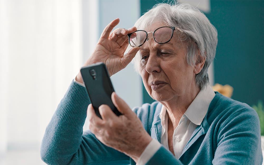 Una mujer se coloca sus gafas para consultar un teléfono móvil