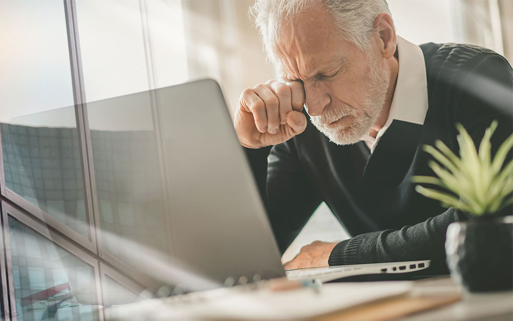 Una persona mayor con gesto de frustración ante un ordenador.
