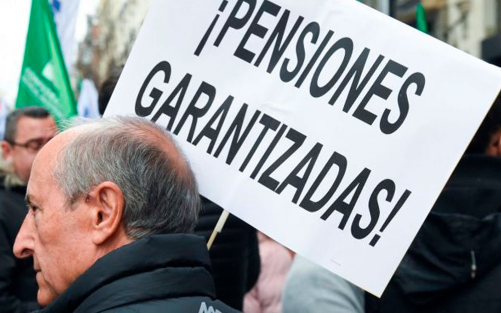 Un apersona en una manifestación sostiene un cartel que dice "Pensiones garantizadas".