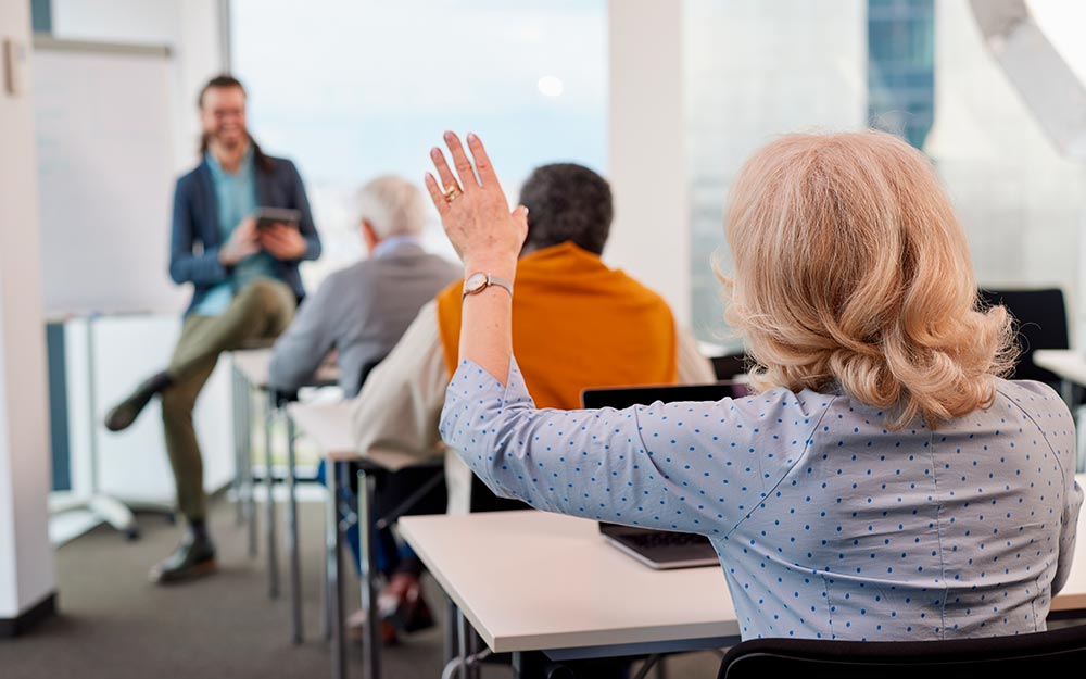 Una mujer levanta la mano en un aula llena de alumnos
