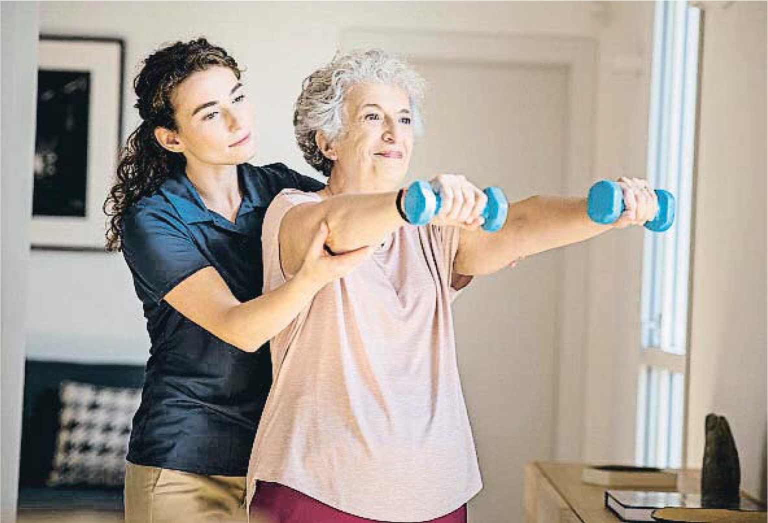 Chica joven ayudando a una mujer mayor a hacer ejercicio con unas mancuernas