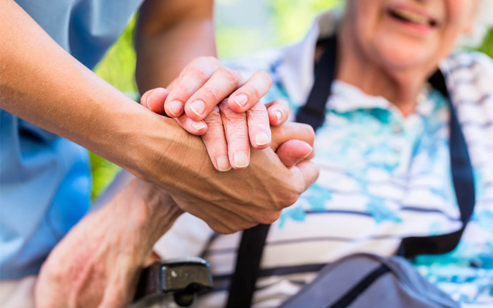 Una persona cuidadora sujeta la mano de una persona mayor.