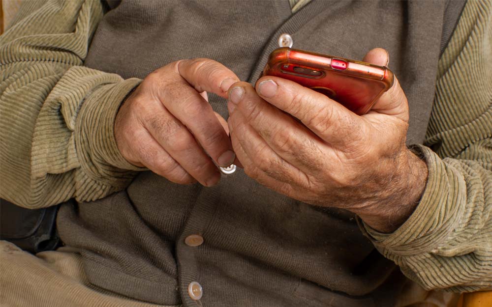 Una persona mayor sostiene un teléfono móvil entre sus manos.
