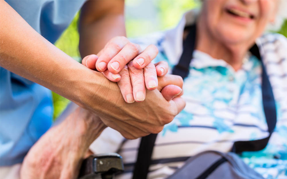 Las manos de una cuidadora sujetan las de una persona mayor.