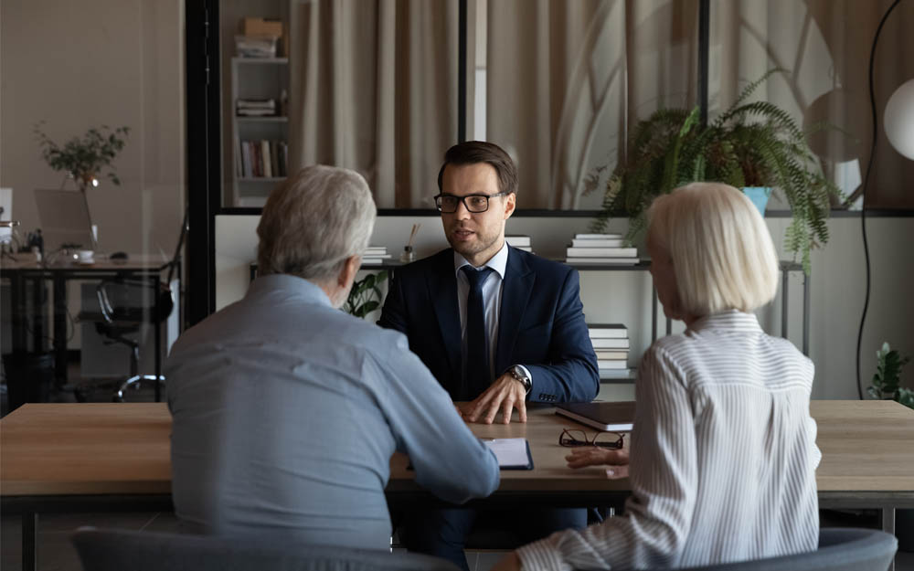 Un profesional de la banca atiende, en una mesa, a dos personas mayores.