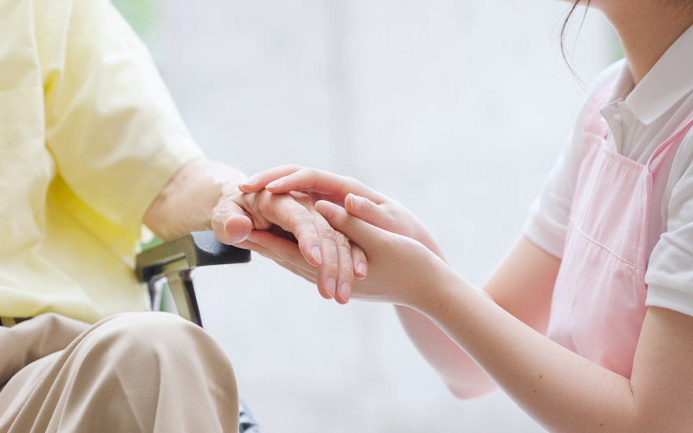 Una persona cuidadora sujeta la mano de una persona mayor.