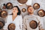 Una pareja de personas tumbada en el suelo con los ojos cerrados y rodeada de cuencos tibetanos