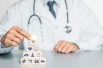Una persona con bata de médico monta una pirámide de bloques de madera con iconos relacionados con la salud