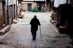 Una mujer mayor con un bastón camina sola por la calle de un pueblo 