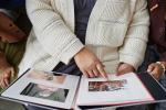 Una persona mayor enseña un álbum de fotos a otras dos personas