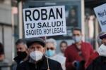 Una persona mayor en una manifestación porta un cartel que dice "roban tu salud, saqueo hoy legal".