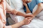 Una persona sujeta la mano de una persona mayor que aparecen tumbada en la cama de un hospital