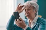 Una mujer se coloca sus gafas para consultar un teléfono móvil