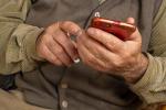 Una persona mayor sostiene un teléfono móvil entre sus manos.