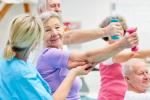 Una persona cuidadora atiende y conversa con una mujer mayor que práctica una actividad física.