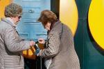 Una mujer mayor, ante un cajero, entrega a otra una libreta bancaria