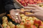 Una persona paga su compra en una frutería. En la imagen, se ven dos manos: una de ellas, con unas monedas; y la otra, a punto de cogerlas.