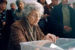 Una mujer mayor observa una urna electoral.