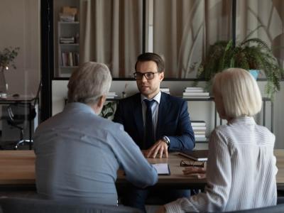 Un profesional de la banca atiende, en una mesa, a dos personas mayores.
