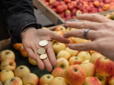 Una persona paga su compra en una frutería. En la imagen, se ven dos manos: una de ellas, con unas monedas; y la otra, a punto de cogerlas.