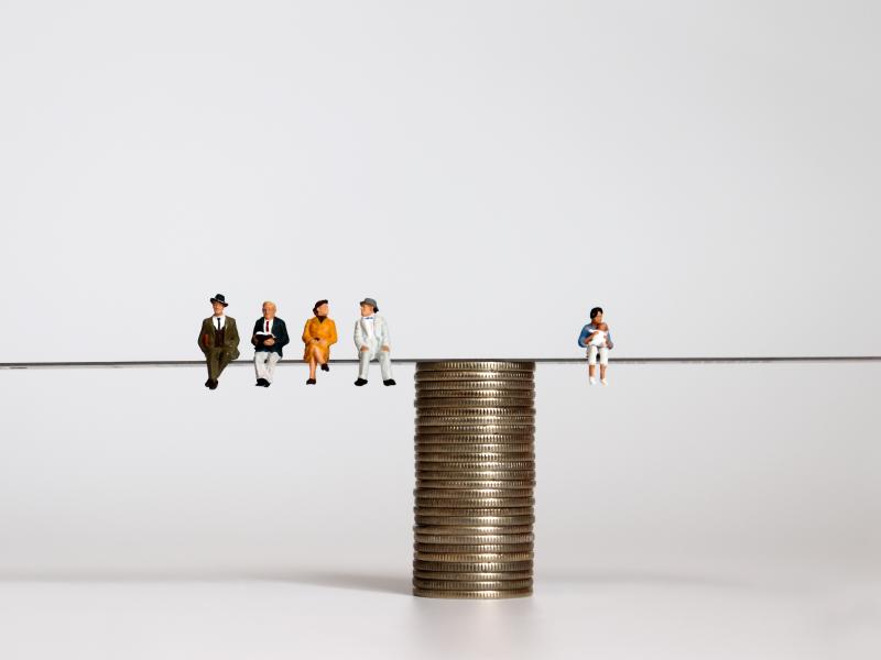 Balanza sobre monedas con una persona a la derecha que representa la población activa y al izquierda personas mayores jubiladas