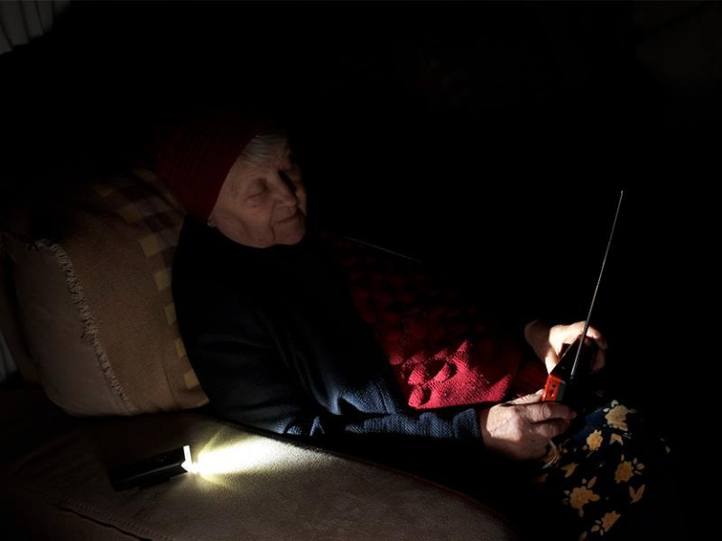 Una mujer sentada sostiene en sus manos un transistor de radio mientras se ilumina con una lintarna 