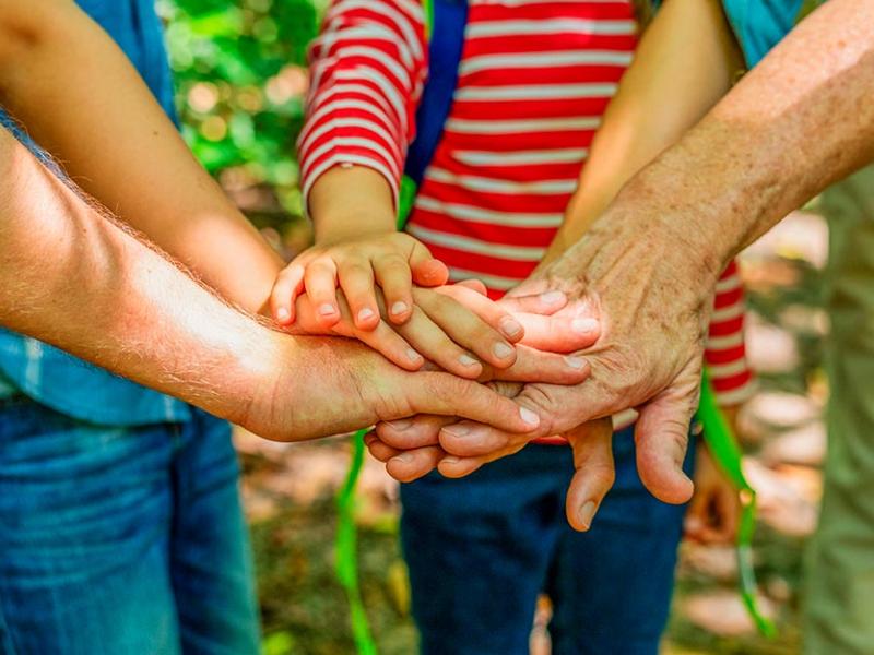 Un grupo de personas de todas las edades unen sus manos en el centro