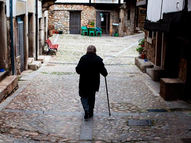 Una mujer mayor con un bastón camina sola por la calle de un pueblo 