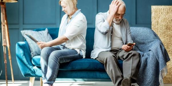 Dos personas mayores en un sofá consultan una tablet y un teléfono móvil