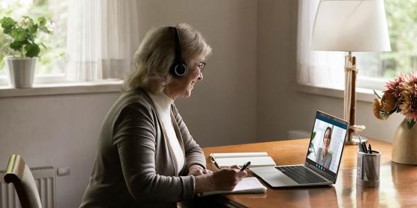 Una mujer toma notas mientras atiende una videoconferencia