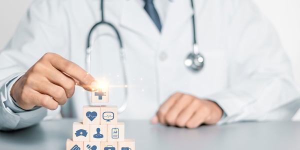 Una persona con bata de médico monta una pirámide de bloques de madera con iconos relacionados con la salud