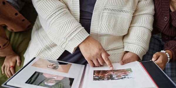 Una persona mayor enseña un álbum de fotos a otras dos personas
